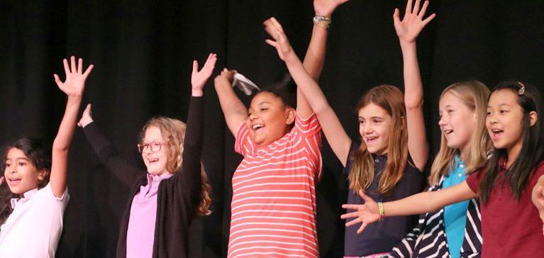 A group of girls at Chase Collegiate throw their hands up in the air laughing during Theater practice.